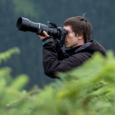 Homem a tirar foto com câmara profissional numa área verde