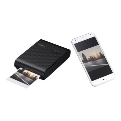 Impressora portátil Canon preta ao lado de smartphone branco com foto de cidade.