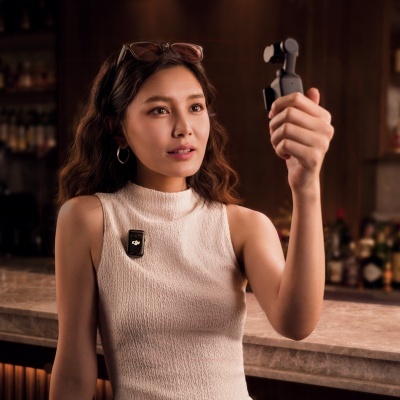 Mulher a segurar pequena câmera cinzenta com estabilizador num bar interior