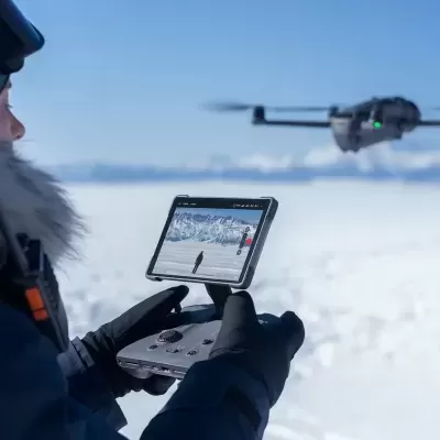 Pessoa a controlar drone com comando ecrã num cenário de neve