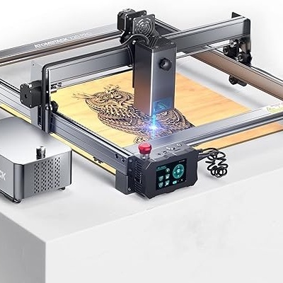 Máquina de gravação a laser preta gravando coruja em madeira clara sobre mesa branca