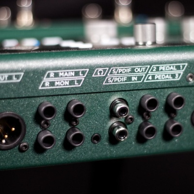 Detalhe das conexões traseiras de um equipamento áudio profissional verde escuro