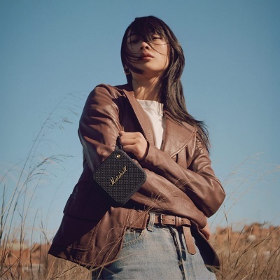 Mulher com casaco de pele castanho e coluna portátil preta Marshall ao ar livre