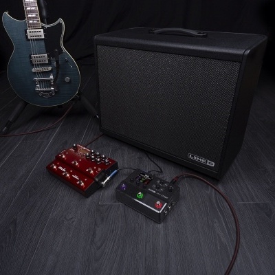 Guitarra elétrica azul com amplificador preto e pedais de efeitos no chão escuro