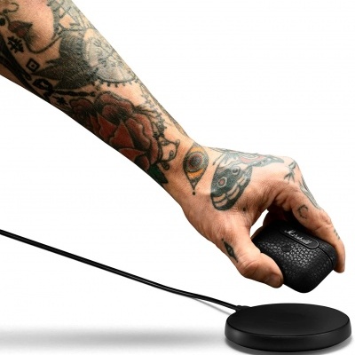 Mão tatuada segurando estojo preto Marshall sobre base redonda preta com cabo