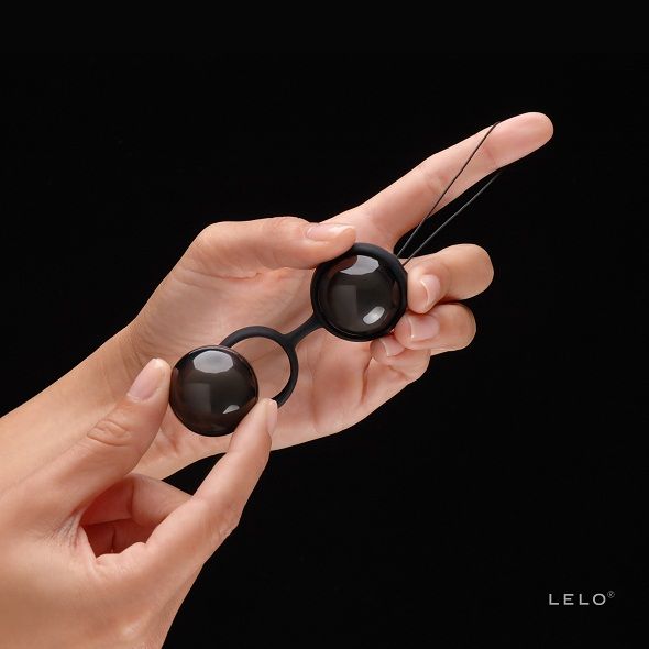 LELO LUNA Beads™ Noir – Bolas Chinesas Elegantes para Exercícios de Kegel Bolas de material preto ligadas, seguradas por mãos com fundo preto e texto LELO