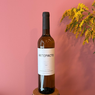 Garrafa de vinho branco com rótulo ARTEFACTO sobre base de cortiça e flores amarelas ao lado