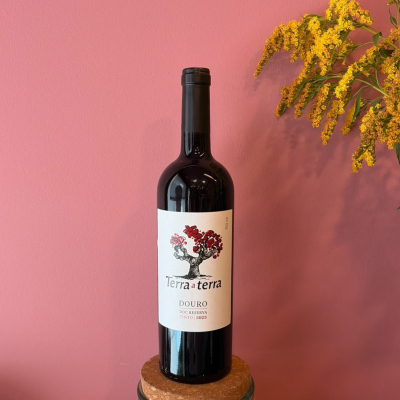 Garrafa de vinho tinto Terra a terra com rótulo branco, apoio de cortiça e flores amarelas ao lado