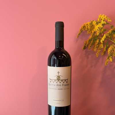 Garrafa de vinho tinto Quinta dos Frades contra parede rosa com flores amarelas