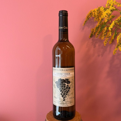 Garrafa de vinho verde com rótulo branco e ilustração de uvas, parede rosa e flores amarelas