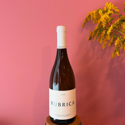Garrafas de vinho tinto com rótulo branco e flores amarelas contra parede rosa