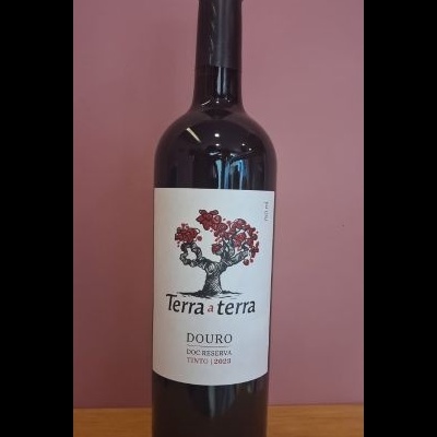 Garrafa de vinho tinto com rótulo branco e desenho de árvore vermelha, texto Terra a terra, Douro DOC Reserva Tinto 2023