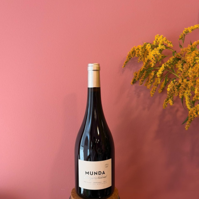 Garrafa de vinho tinto com rótulo branco e flores amarelas ao lado sobre fundo rosa