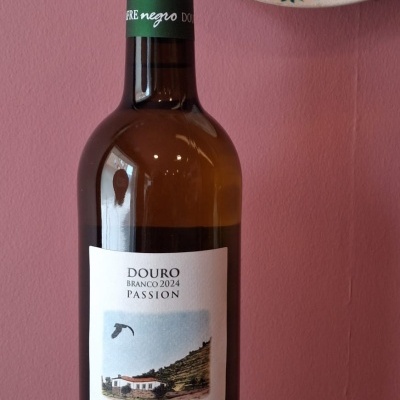 Garrafa de vinho branco Milhafre negro com rótulo branco e texto, junto a prato decorativo