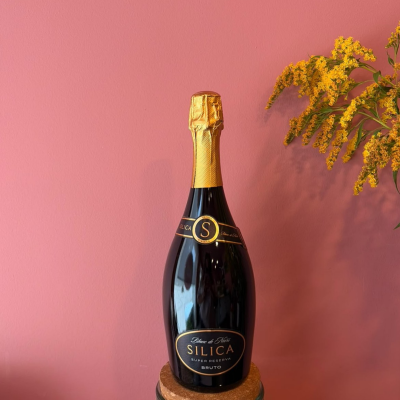 Garrafa de champanhe preta com rótulo preto e dourado e flores amarelas ao lado