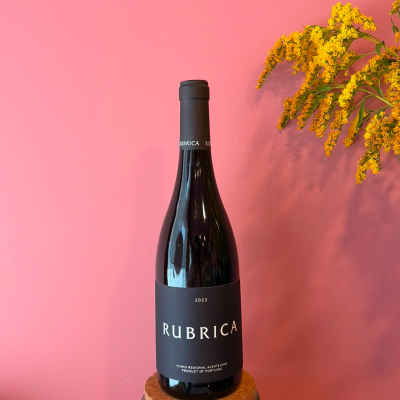 Garrafa de vinho tinto Rubrica 2022 com rótulo preto em fundo rosa e flores amarelas