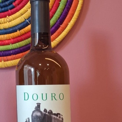 Garrafa de vinho branco Douro Pouca Terra 2024 com rótulo e decoração colorida ao fundo