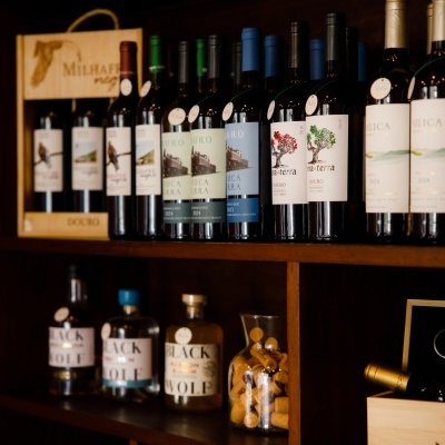 Garrafas de vinho variadas em estante de madeira escura com jarra de rolhas
