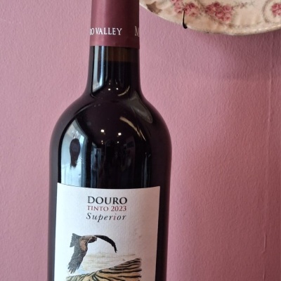 Garrafa de vinho tinto Douro 2023 Milhafre Negro com fundo rosa e prato decorativo