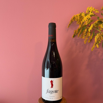 Garrafa de vinho tinto com rótulo branco e texto fagote Reserva DOURO TINTO 2022 750 ml ao lado de flores amarelas, fundo rosa