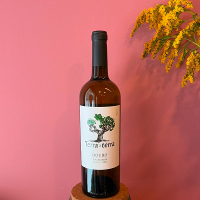 Garrafa de vinho branco Douro Terraterra sobre suporte com parede rosa e flores amarelas ao lado