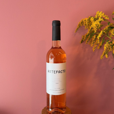 Garrafa de vinho rosé com rótulo branco, tampo preto, base de cortiça, fundo rosa e flores amarelas