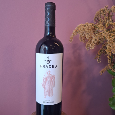 Garrafa de vinho tinto Frades Douro 2023 com flores secas e fundo rosa