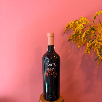 Garrafa de vinho preta com tampa rosa em suporte de cortiça, parede rosa e flores amarelas