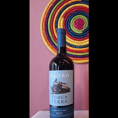 Garrafa de vinho Douro Pouca Terra 2023 frente a parede rosa com decoração colorida redonda