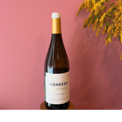 Garrafa de vinho branco com rótulo branco e tampa branca, suporte de cortiça, flores amarelas e fundo rosa.