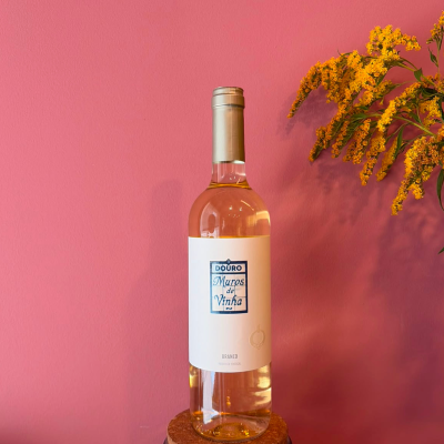 Garrafa de vinho branco com rótulo branco e tampa prata, parede cor-de-rosa, flores amarelas