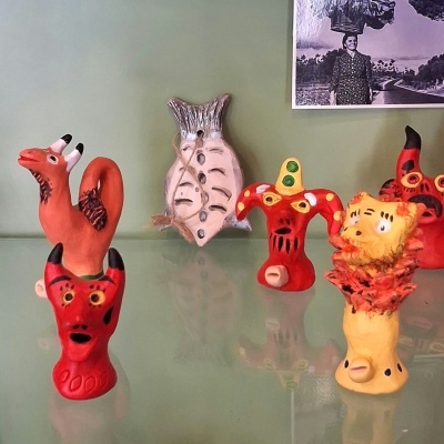Estatuetas coloridas em cerâmica sobre superfície reflexiva e parede verde claro.