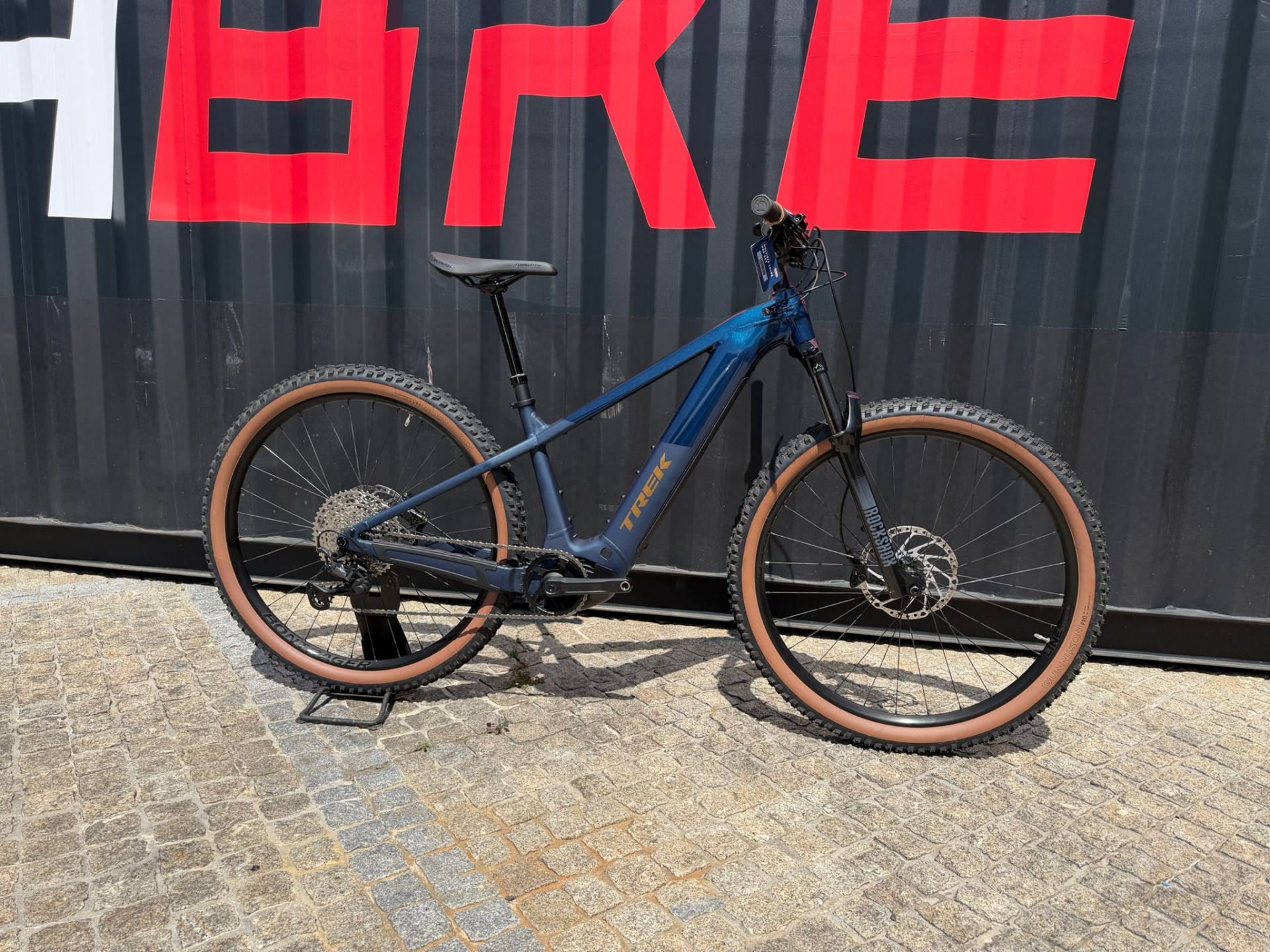 Bicicleta Exposição Trek Powerfly 6 800wh Azul M Bicicleta de montanha elétrica azul Trek com pneus castanhos junto a contentor preto com letras vermelhas