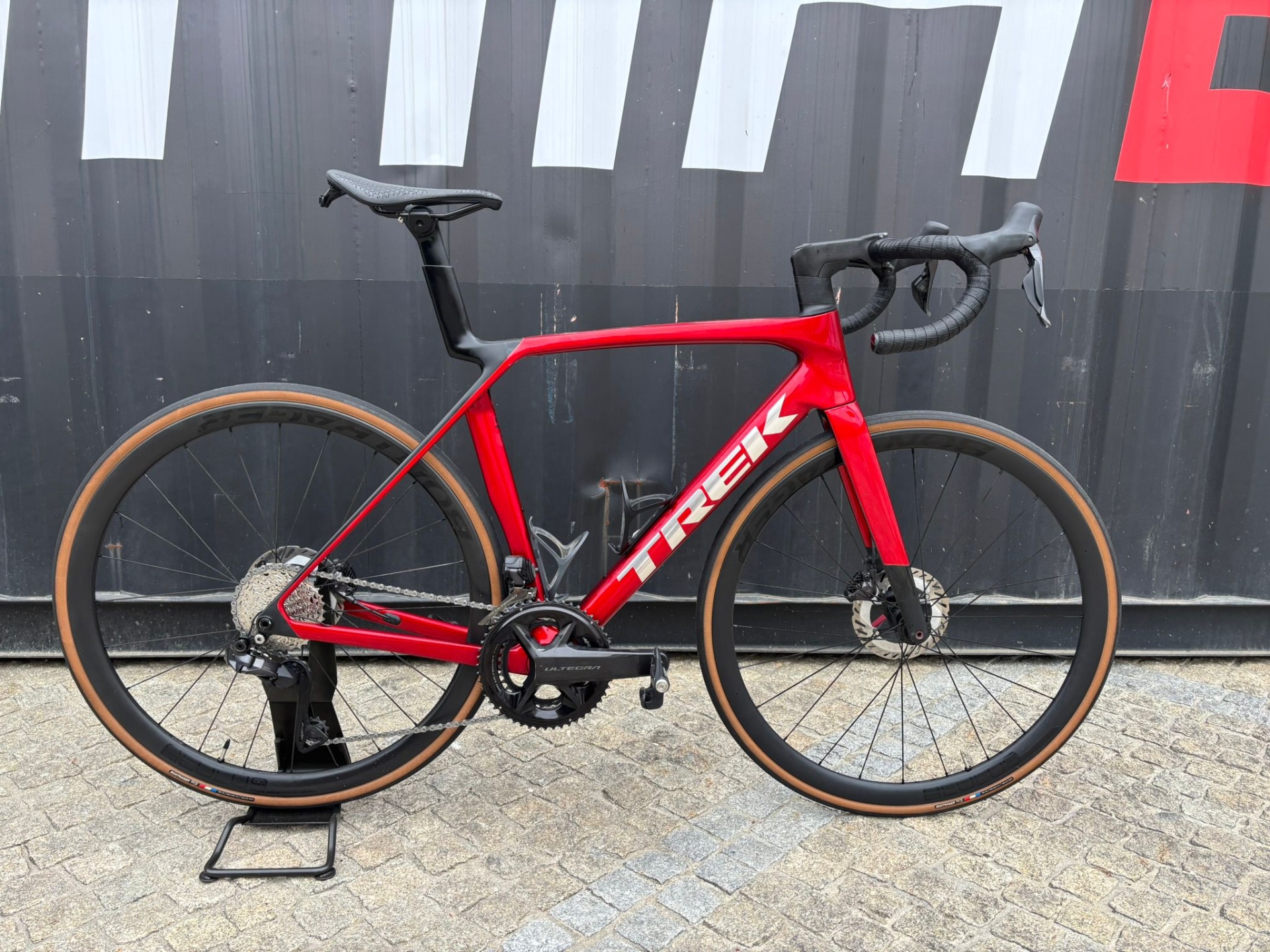 Trek Madone SL 7 de Serviço M/L Bicicleta de estrada vermelha e preta com pneus castanho claro e quadro com o texto TREK.