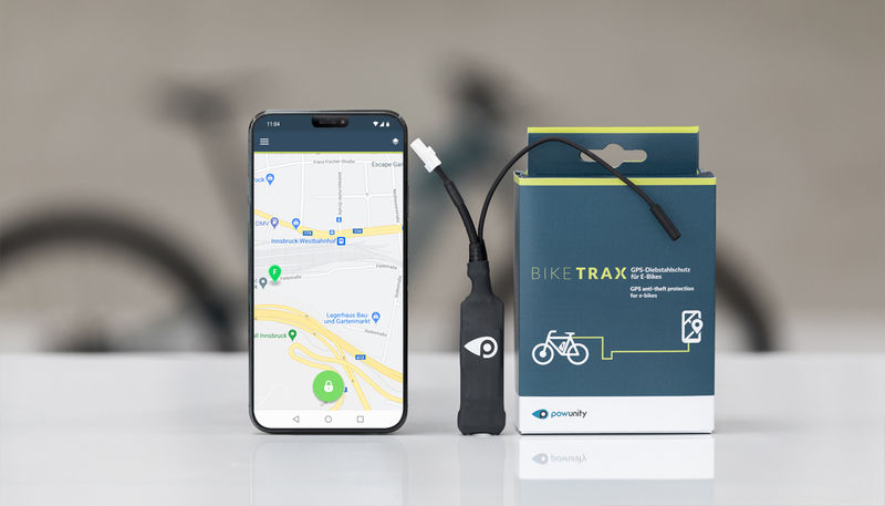 Dispositivo BIKER TRAX ao lado de smartphone com aplicação de mapa aberto sobre superfície branca.