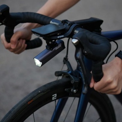 Bicicleta de estrada com luz dianteira e painel digital, guiador preto e mãos segurando