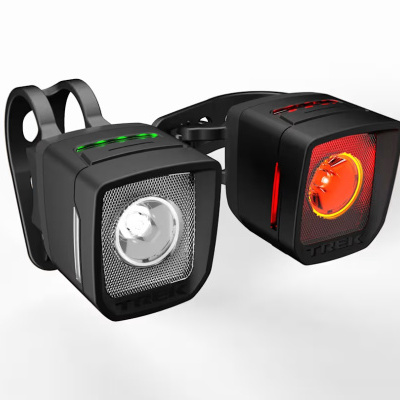 Par de luzes para bicicleta com lente branca à frente e vermelha atrás, LED verde e vermelho em cima, marca TREK.