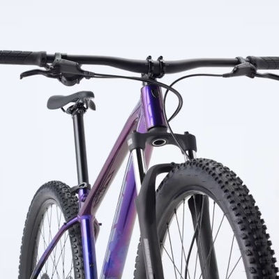 Bicicleta de montanha roxa com pneus cravados e guiador preto num fundo branco