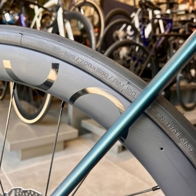 Roda de bicicleta com aro de carbono e pneu preto mostrando texto de especificações em loja.