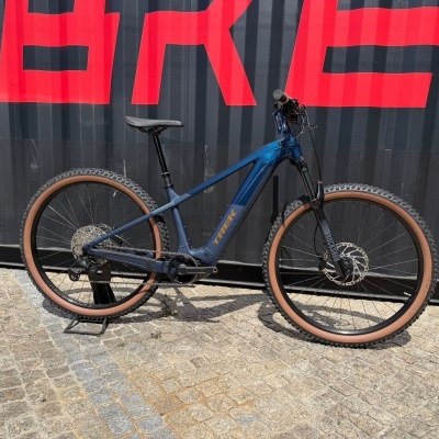 Bicicleta de montanha elétrica azul Trek com pneus castanhos junto a contentor preto com letras vermelhas