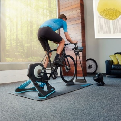 Homem a usar bicicleta de treino indoor num rolo azul e preto dentro de casa