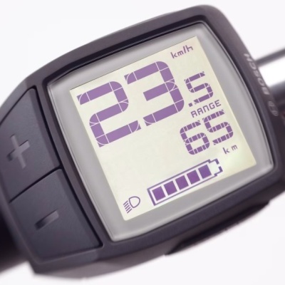 Painel de controlo digital preto com ecrã a mostrar velocidade, alcance e nível de bateria