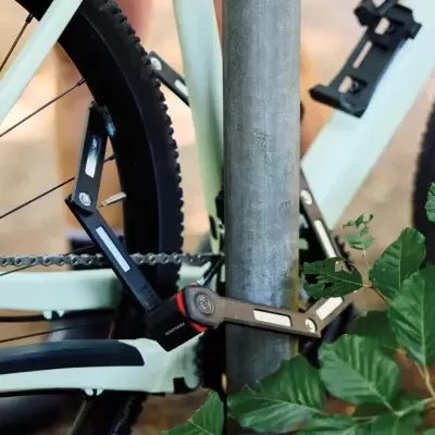 Fecho dobrável preto para bicicleta em poste metálico com bicicleta branca ao fundo