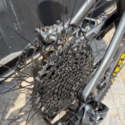 Detalhe da roda traseira de uma bicicleta cinzenta com engrenagem preta e sistema de travagem metálico.