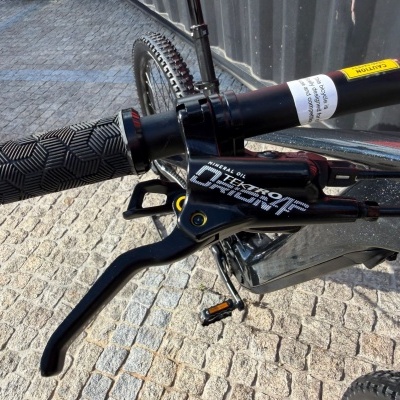 Manípulo de bicicleta preto com padrão em hexágonos, alavanca de travão Tektro Orion e etiquetas de aviso na barra do guiador