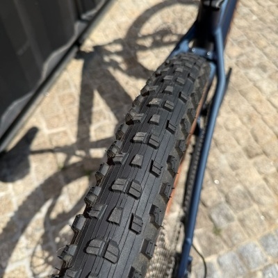 Pneu preto de bicicleta com padrão de cravos numa roda azul escura sobre calçada de pedra.