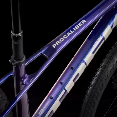 Parte da estrutura metálica azul e roxa de uma bicicleta com o nome PROCALIBER e pneus pretos