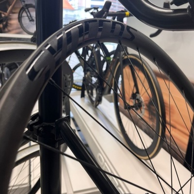 Roda de bicicleta em carbono preto com inscrição SYNTHOS e quadro preto em loja de bicicletas