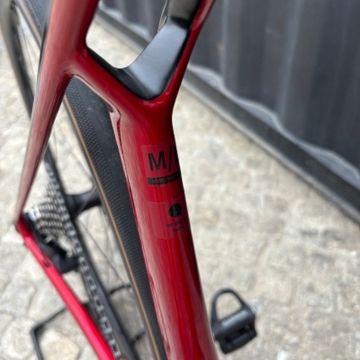 Quadro de bicicleta vermelha com autocolante M/L ISO 4210-2 Racing e roda ao fundo.