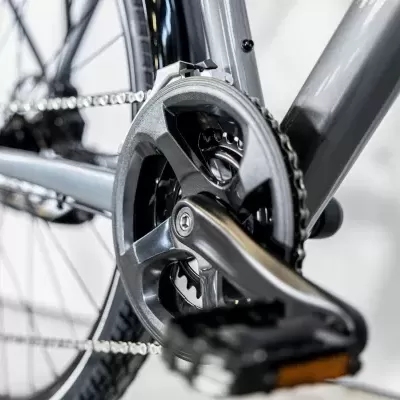 peça de bicicleta com pedaleira preta e corrente prateada num quadro cinzento metálico